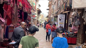 Zwei Jungen gehen durch eine belebte Gasse, umgeben von bunten Souvenirläden und Handwerksständen.