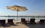 Ein ruhiger Blick auf eine Terrasse mit Liegen, einem Sonnenschirm und dem Nil im Hintergrund unter klarem Himmel.