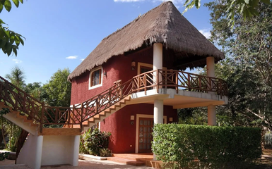 Ein zweigeschossiges, rot gestrichenes Gebäude mit einem Strohdach und Holzgeländer, umgeben von üppigem Grün.