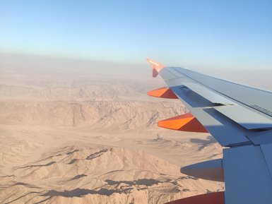 Der Blick aus dem Flugzeug zeigt die schroffen, braunen Berge und das klare, blaue Himmel über einer weiten Wüstenlandschaft.