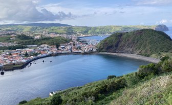 Eine malerische Küstenlandschaft mit einer Stadt, umgeben von sanften Hügeln und einem ruhigen, blauen Meer.