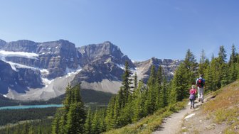 Ein Wanderer und ein Kind erkunden einen malerischen Pfad in den Rocky Mountains, umgeben von majestätischen Bergen und Nadelbäumen.