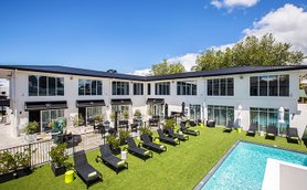 Ein modernes Boutique-Hotel mit einem einladenden Poolbereich und Liegen auf grünem Rasen unter blauem Himmel.
