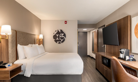 Ein modernes Hotelzimmer mit einem großen Bett, einem Schreibtisch und einem Fernseher an der Wand.