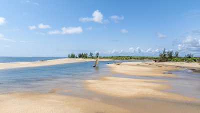 Ein ruhiger Strand mit feinem Sand und sanften Wellen, während ein traditionelles Boot in der Nähe der Küste segelt.