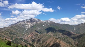 Die majestätischen Chimgan-Berge erheben sich unter einem strahlend blauen Himmel mit weißen Wolken und schneebedeckten Gipfeln.