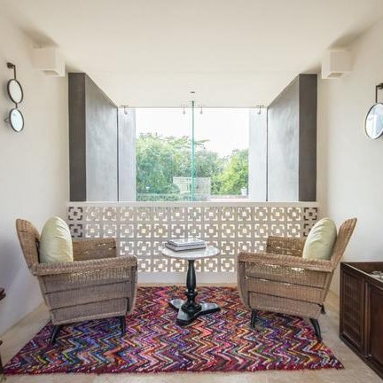 Ein einladender Raum mit zwei Korbstühlen, einem Tisch und einem bunten Teppich, der eine entspannte Atmosphäre schafft.