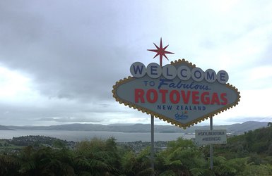 Ein farbenfrohes Willkommensschild für Rotovegas, umgeben von einer malerischen Landschaft und einem bewölkten Himmel.