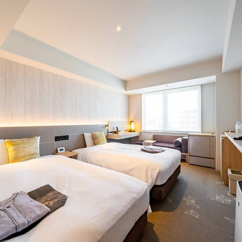 Ein modernes Hotelzimmer mit zwei Einzelbetten, einem großen Fenster und einem gemütlichen Sitzbereich im Hintergrund.