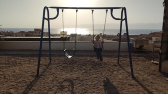 Ein Kind schwingt fröhlich auf einer Schaukel, während die Sonne über dem Meer untergeht und die Landschaft erleuchtet.