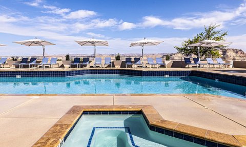 Ein glitzernder Pool mit Liegen und Sonnenschirmen, umgeben von einer atemberaubenden Landschaft und klarem Himmel.