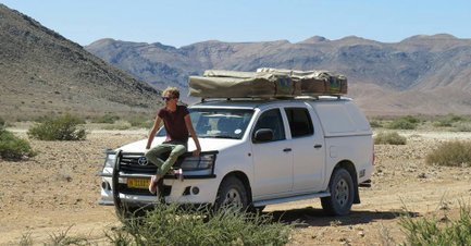 Ein Mann sitzt auf einer Motorhaube eines Jeeps mit einem Dachzelt - Namibia Familienurlaub