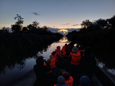 Eine Gruppe von Menschen in orangefarbenen Schwimmwesten fährt auf einem ruhigen Wasserweg bei Sonnenuntergang.