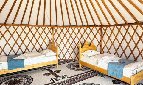 Ein traditionelles mongolisches Jurteninnere mit zwei Betten, die mit weißen Kissen und einer blauen Decke dekoriert sind.