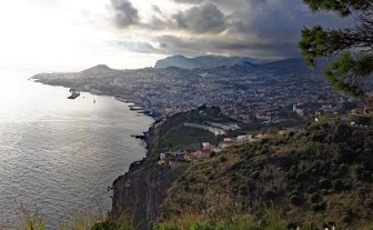 Ein atemberaubender Blick auf die Küste von Funchal, Madeira, mit dramatischen Wolken und sanften Hügeln im Hintergrund.