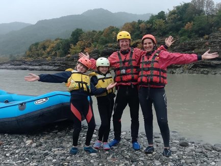 Eine fröhliche Familie posiert am Ufer eines Flusses, bereit für ein aufregendes Rafting-Abenteuer in der Natur.
