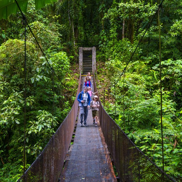 Eine Familie überquert eine Hängebrücke inmitten üppiger, grüner Vegetation in Costa Rica.