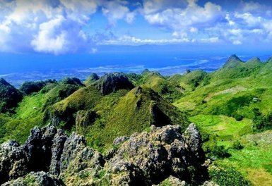 Eine atemberaubende Aussicht auf die grünen Hügel und das blaue Meer von Osmena Peak unter einem klaren Himmel.