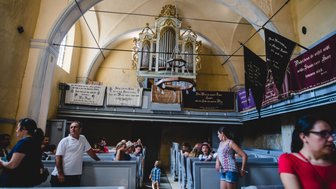 Eine helle Kirche mit einer beeindruckenden Orgel im Hintergrund, während Besucher in den Bänken sitzen und sich unterhalten.