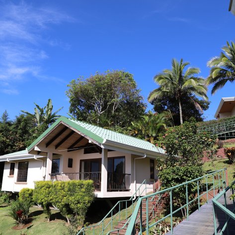 Ein charmantes Hotelgebäude mit grünem Dach, umgeben von üppiger Vegetation und strahlend blauem Himmel.