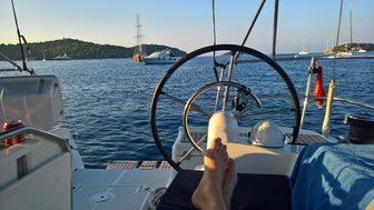 Ein entspannter Moment auf einem Segelboot, mit Blick auf das ruhige Wasser und die sanften Hügel im Hintergrund.