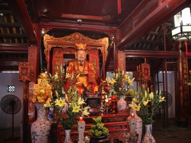 Ein prächtiger, goldener Altar mit einer Statue eines lächelnden Mannes, umgeben von üppigen Blumen und Kerzenlicht.