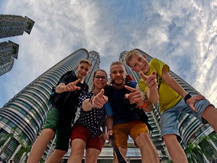 Familie posiert fröhlich für ein Selfie mit den Petronas Twin Towers im Hintergrund – Malaysia & Borneo Reise mit Kindern