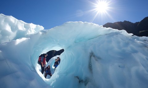 Eine Gruppe von Wanderern erkundet eine beeindruckende Eishöhle unter strahlend blauem Himmel und hellem Sonnenlicht.