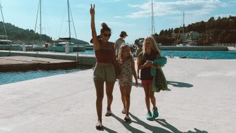Eine fröhliche Familie spaziert am Hafen entlang, umgeben von Segelbooten und strahlend blauem Himmel.
