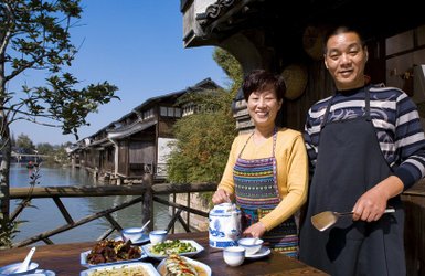 Ein fröhliches Paar steht am Ufer eines malerischen Flusses und präsentiert eine Auswahl an köstlichen Gerichten.