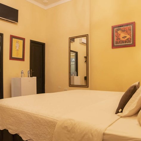 Ein gemütliches Zimmer mit einem großen Bett, einem Spiegel und bunten Bildern an den Wänden, das eine einladende Atmosphäre schafft.