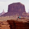 Drei Personen stehen auf einer Felsplattform in Monument Valley, umgeben von beeindruckenden roten Felsen und Hügeln.