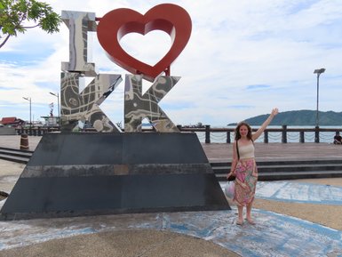 Mädchen steht stolz neben dem bekannten Kota Kinabalu Schriftzug – Malaysia & Borneo Reise mit Kindern