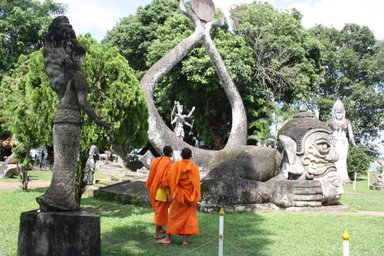 Zwei Mönche in orangefarbener Robe stehen vor einer beeindruckenden Statue eines liegenden Buddhas im Buddha-Park.