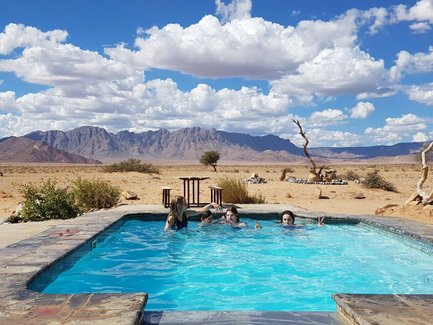 Eine Gruppe von Menschen entspannt im Pool, umgeben von einer beeindruckenden Wüstenlandschaft und Bergen im Hintergrund.