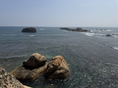 Eine ruhige Küstenlandschaft mit großen Felsen, die im klaren Wasser stehen, während sanfte Wellen an die Küste schlagen.