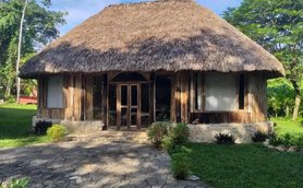 Ein traditionelles, strohgedecktes Haus aus Holz steht in einer grünen Umgebung mit einem gepflasterten Weg davor.