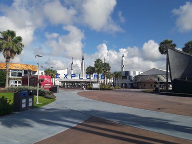 Ein sonniger Tag am Kennedy Space Center mit dem großen 'EXPLORE'-Schild und Raketen im Hintergrund.