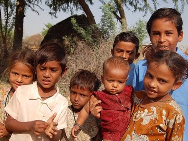 Eine Gruppe von sieben Kindern steht zusammen im Freien, umgeben von Natur und einem ländlichen Hintergrund.