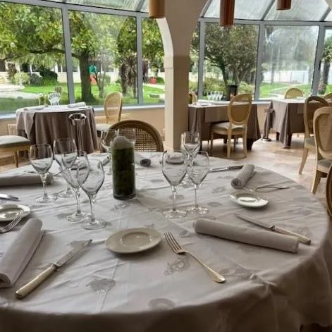 Ein eleganter Tisch mit Gläsern und Besteck, umgeben von einem hellen Restaurant mit Blick auf einen Garten.