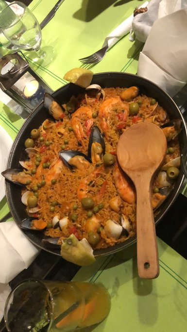 Ein köstlicher Teller Paella mit Garnelen, Muscheln und Erbsen, serviert in einer großen Pfanne auf einem grünen Tisch.