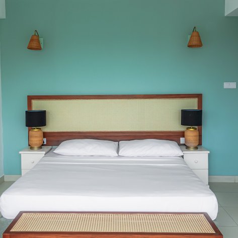 Ein helles Schlafzimmer mit einem großen Bett, zwei Nachttischlampen und einer sanften aquamarinfarbenen Wand.