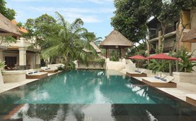 Ein ruhiger Poolbereich in Bali, umgeben von tropischen Pflanzen und Sonnenliegen unter roten Sonnenschirmen.
