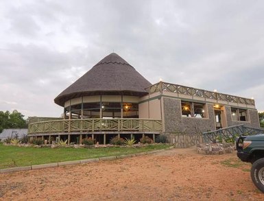 Ein modernes Safari-Lodge-Gebäude mit einem markanten, strohgedeckten Dach und einer einladenden Veranda umgeben von Pflanzen.