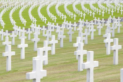 Eine weite Ansicht eines Friedhofs mit zahlreichen weißen Kreuzen, die in sanften Bögen auf grünem Gras angeordnet sind.