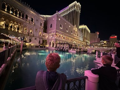 Zwei Kinder stehen am Ufer eines beleuchteten Kanals in Las Vegas, während sie die beeindruckende Architektur bewundern.