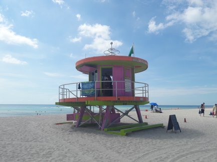 Ein lebhaftes, pinkfarbenes Rettungsschwimmerhaus steht am Strand von Miami, umgeben von feinem Sand und klarem Wasser.