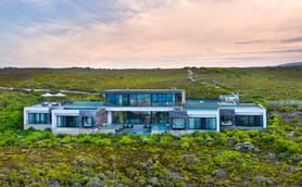 Ein modernes, elegantes Haus mit großen Fenstern steht inmitten einer üppigen, grünen Landschaft unter einem sanften Himmel.