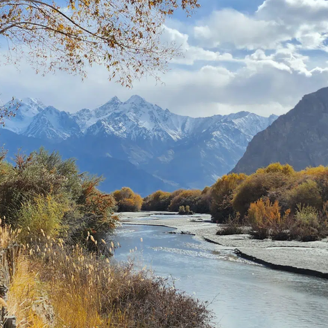 Ein ruhiger Fluss schlängelt sich durch eine herbstliche Landschaft, umgeben von schneebedeckten Bergen und buntem Laub.
