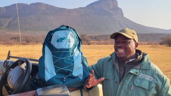 Ein freundlicher Guide steht neben einem For Family Reisen-Rucksack und lacht in die Kamera – Südafrika mit Kindern